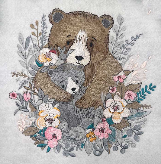 Embroidered artwork of a mother bear hugging her cub surrounded by soft floral and leafy details in muted tones with pink and cream flowers, original EmbroMania design.