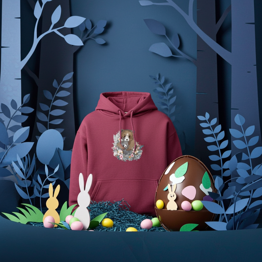 Burgundy premium hoodie with mother bear and cub floral embroidery, styled in a whimsical forest scene with Easter eggs and bunny decor, original EmbroMania artwork.