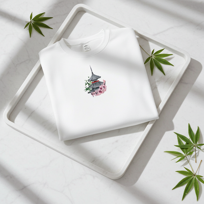 White unisex crewneck sweatshirt with pagoda and sakura cherry blossom embroidery design, flat lay on marble table with plant and soft sunlight.
