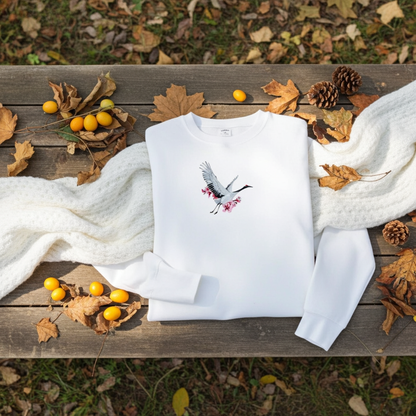 White unisex crewneck sweatshirt with sakura crane embroidery design, flat lay with cozy scarf, autumn leaves, pinecones and berries.