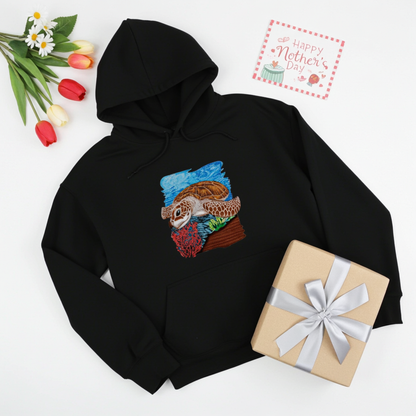 Black premium hoodie with Sea Turtle & Coral Reef embroidery showing a sea turtle above red coral and green sea plants on a blue ocean background, styled with tulips, a Mother’s Day card, and a wrapped gift, original EmbroMania artwork.