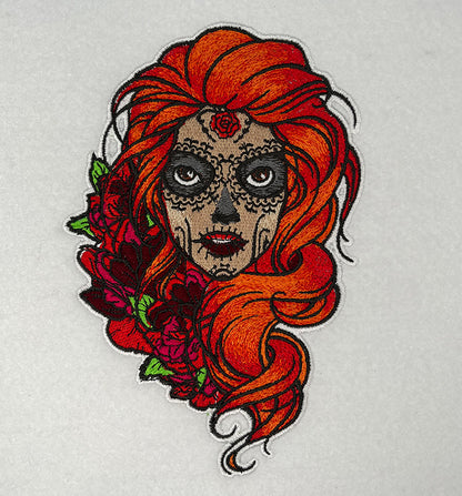 Embroidered sugar skull girl portrait with bright orange hair, detailed skull makeup, and red roses, bold Día de los Muertos inspired design, original EmbroMania artwork.