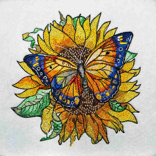 Embroidered butterfly with blue and orange wings resting on a large golden sunflower with green leaves, bright nature-inspired design, original EmbroMania artwork.