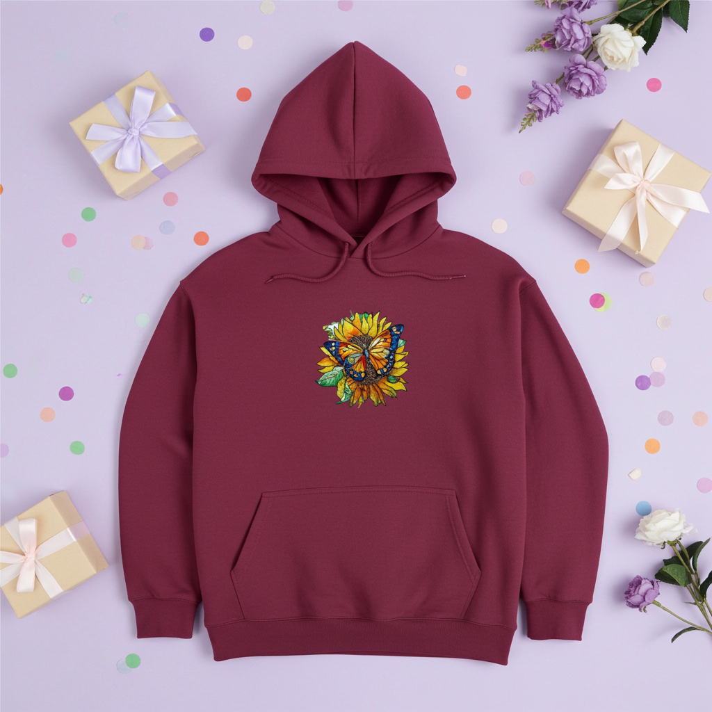 Burgundy premium hoodie with Sun-Kissed Butterfly & Sunflower embroidery featuring a blue and orange butterfly on a golden sunflower with green leaves, styled on a purple background with confetti, flowers, and gift boxes, original EmbroMania artwork.