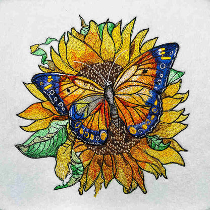 Embroidered design  featuring a colorful butterfly sitting on a sunflower with surrounding green leaves.