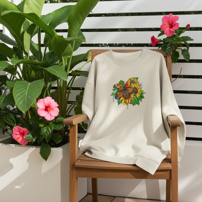 Mint green  unisex crewneck sweatshirt with sunflower and butterfly embroidery design, styled on wooden chair outdoors with green plants and pink flowers.
