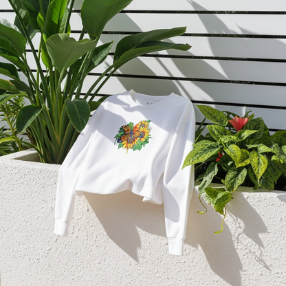 White unisex crewneck sweatshirt with sunflower and butterfly embroidery design, styled outdoors on wall ledge with green plants and sunlight.