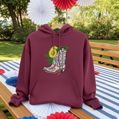 Burgundy unisex pullover hoodie with sunflower cowboy boots appliqué embroidery design, styled outdoors on table with festive paper decorations.