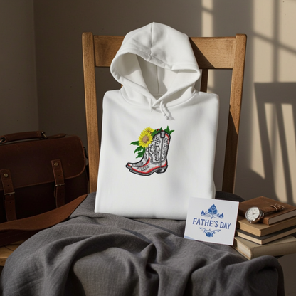 White hoodie mockup with embroidered cowboy boot and sunflower appliqué on the chest, styled on a wooden chair with books and a Father’s Day card.
