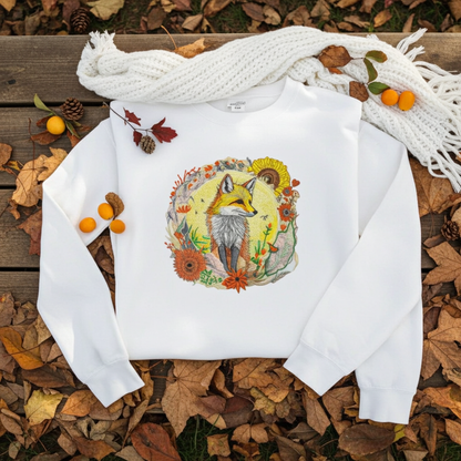 White unisex crewneck sweatshirt with sunlit fox and floral embroidery design, flat lay with autumn leaves, scarf, pinecones and berries.