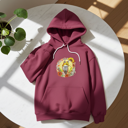 Burgundy premium hoodie with Sunshine Fox & Sunflower embroidery featuring a fox framed by sunflowers and wildflowers in warm tones, laid flat on a white round table in bright natural light with a potted plant, original EmbroMania artwork.