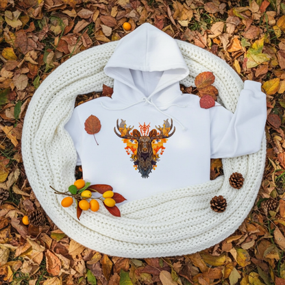 White premium hoodie with Tribal Fire Moose embroidery featuring a moose head with bold antlers and tribal details in warm orange and brown tones, styled on a white knit blanket with autumn leaves, pinecones, and small orange berries, original EmbroMania artwork.