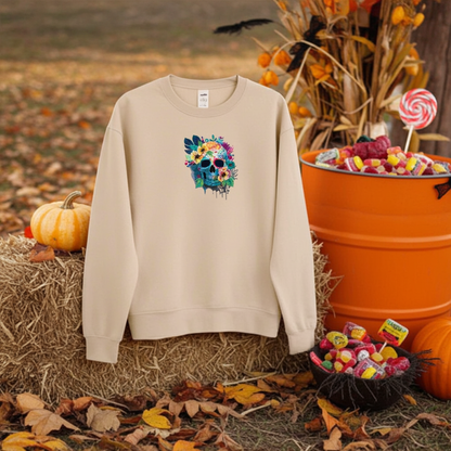 Soft beige sweatshirt displayed on a hay bale outdoors, featuring a colorful floral blue skull embroidery on the chest, styled with pumpkins, fall leaves, and Halloween candy in the background