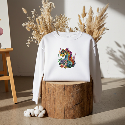 White unisex crewneck sweatshirt with vivid bloom dragon embroidery design, styled on wooden stump with dried florals in studio setting.