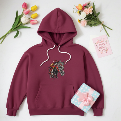 Burgundy unisex pullover hoodie with wild spirit horse head embroidery in black, red and gold, flat lay with flowers, gift box and Mother’s Day card.