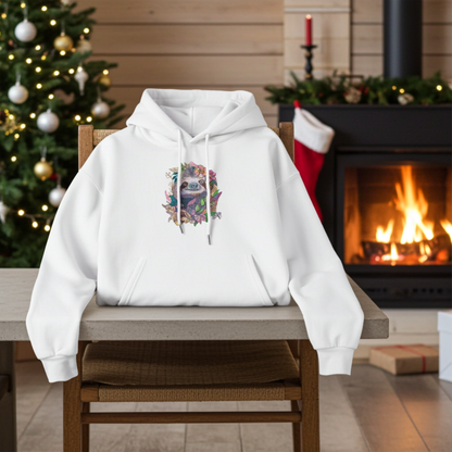 White hoodie mockup featuring a floral sloth embroidered design on the chest, styled on a chair in a cozy Christmas living room with a lit fireplace and decorated tree.