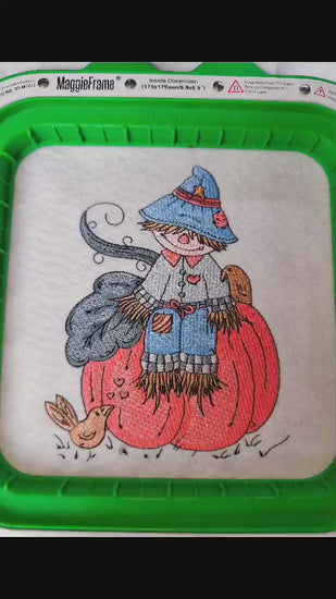 Embroidered fall design featuring a cute scarecrow with a blue hat and patchwork clothes sitting on a pumpkin, surrounded by birds and autumn leaves. Perfect for hoodies, sweatshirts, and tote bags.